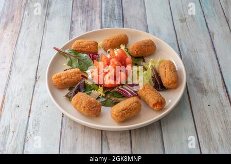 Teller mit Kroketten gefüllt mit gebratenem Huhn mit Béchamelsauce mit Sprossen und Tomatensalat auf einem weißen Teller Stockfoto