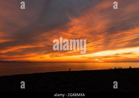 Spektakuläre Aussicht auf Reisende Silhouetten betrachten Meer vom Strand unter bunten bewölkten Himmel bei Sonnenuntergang Stockfoto