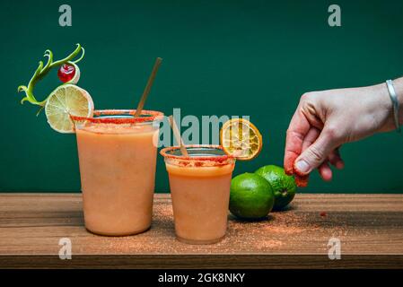 Mexikanischer Vampir-Cocktail in Plastikbechern mit Männerhand-Dressing die Getränke sind Salz und Gewürze, Limette, Zitrone und Orange Stockfoto