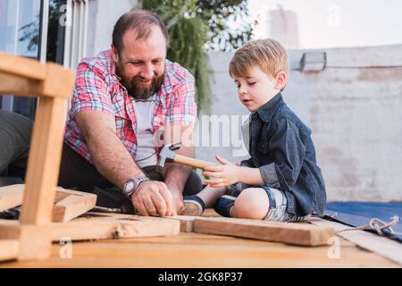Bärtiger Vater unterrichtete Sohn mit Hammer, der am Wochenende auf der Promenade mit Holz arbeitete Stockfoto