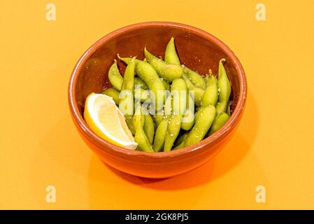 Tonschüssel mit Edamamaboden mit Flakensalz und einem Zitronenkeil zum Verzieren. Stockfoto