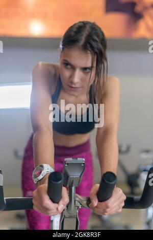 Konzentrierte schweißtreibende junge Sportlerin in der oberen und Legging dabei Cardio-Training auf dem Heimtrainer im Fitnessstudio Stockfoto