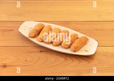 Köstliche spanische Tapa aus hausgemachten Kroketten paniert und gefüllt mit Creme mit iberischem Schinken auf einem Holztisch Stockfoto