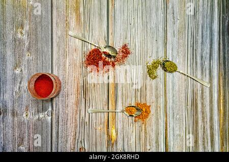 Metalllöffel mit Gewürzen auf Holztisch umgedreht. Paprika und Paprika aus la Vera, rotem Paprika und Orangano Stockfoto