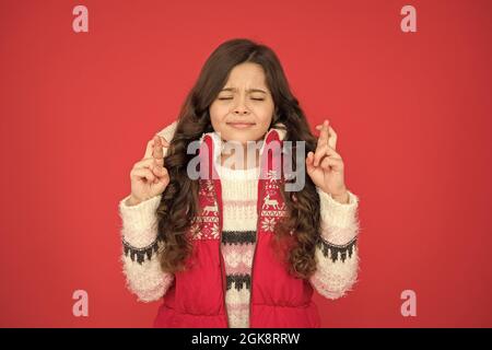 Teen Mädchen mit langen lockigen Haaren machen einen Wunsch tragen Kugelweste und Pullover mit weihnachtsmustern, Neujahr Wunsch Stockfoto