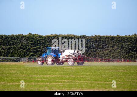 Canterbury, Neuseeland, September 11 2021: Ein Traktor aus New Holland mit angeschlossenem Atlas-Feldspritzer sprüht im Frühjahr eine Feldfrucht Stockfoto