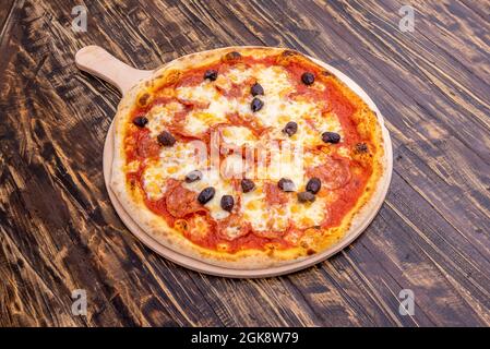 Super Diavola Pizza mit schwarzen Oliven, würzigen Pfefferoni, Mozzarella-Käse und Tomaten auf dunklem Holztisch. Stockfoto