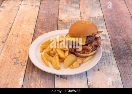 Double Beef Burger mit gebratenem Speck, geschmolzenem Cheddar-Käse mit Tomate und Senf garniert mit Pommes frites Stockfoto