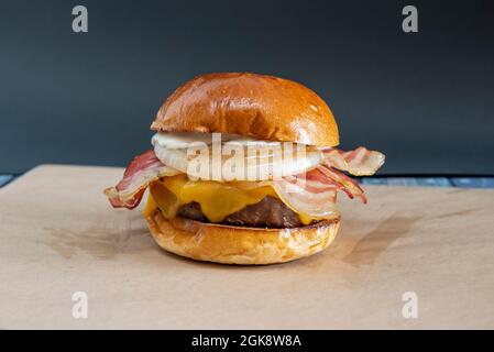 Toller klassischer Burger, der auf dem Grill zubereitet wird, mit viel gebratenem Speck, knusprigen weißen Zwiebelscheiben, geschmolzenem Cheddar-Käse, Mayonnaise und Rindfleisch Stockfoto