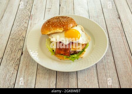 Klassischer Rindfleischburger mit Spiegelei zum Eintauchen des Eigelbs und gebratenen Backs mit geschmolzenem Käse, Salat und Ketchup auf einen weißen Teller Stockfoto