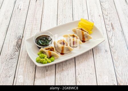 Asiatische Knödel gefüllt mit Fleisch mit Sojasauce und Edamamabohnen, geriebener gelber Pfeffer auf einem weißen Tablett Stockfoto