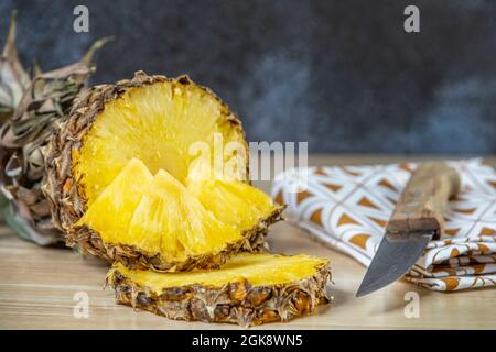 Wunderbare reife Ananas in zwei Hälften geschnitten, Scheiben und Stücke fertig zum Pecken. Reife Früchte mit einem Holzgriffmesser gehackt Stockfoto