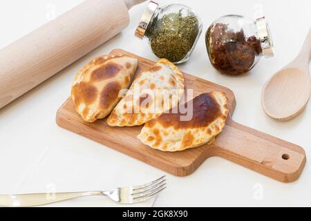 Argentinische Empanadas auf Holzbrett mit Gewürzen und dehydrierten Tomaten mit weißem Hintergrund Stockfoto