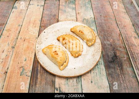 Drei argentinische Hähnchenempanadas auf einem weißen Teller und Holzboden Stockfoto