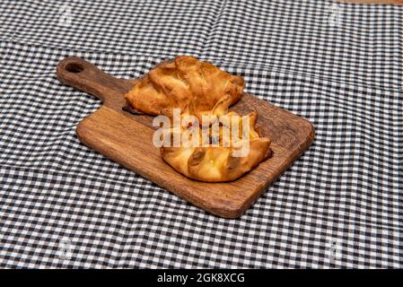 Argentinischer Spinat- und Thunfisch-Empanadas mit Holzbrett auf schwarzer und weißer Tischdecke Stockfoto