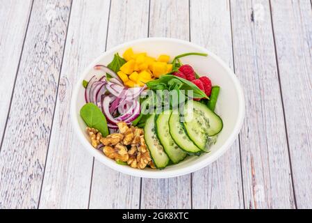 Weiße Pappschale mit Obst und Spinatsalat. Rote Himbeeren, gehackter Mango und rote Zwiebel mit kalifornischen Walnüssen und Gurke SLI Stockfoto