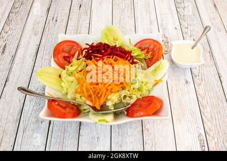 Salat aus Tomaten, Gurken, Eisbergsalat, geriebenen Karotten, geriebenen Rüben und Mayonnaise-Sauce auf weißem Tisch. Stockfoto