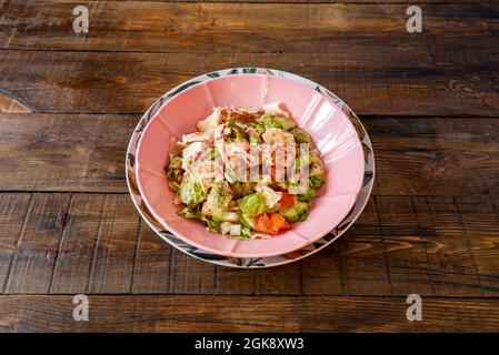 Rosa Schüssel mit mediterranem Salat aus Eisbergsalat, gegrilltem Hähnchen, Gurken, gehackten Tomaten und mit Paprika beträufelt Stockfoto