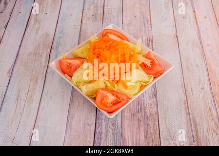 Salat mit Tomaten, geschälten und gehackten Gurken, Eisbergsalat und vielen geriebenen Karotten auf einer quadratischen weißen Schüssel Stockfoto