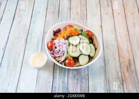 Weiße Schüssel mit Gemüsesalat, Kirschtomaten, rohen roten Zwiebeln, geriebenen Karotten und Salatsprossen Stockfoto