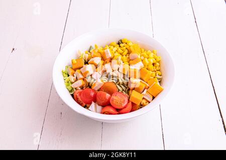 Nudelsalat mit Kirschtomaten, gehackter Surimi, Eisbergsalat und süßem Mais in einer weißen Schüssel. Stockfoto