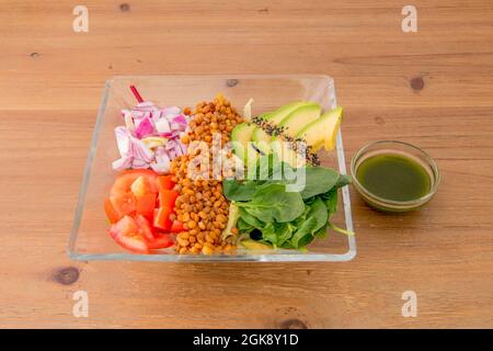 Salat mit mediterranen und amerikanischen Zutaten. Grün-gelbe Avocado, grüner Spinat, rote Zwiebel, geschmorte Linsen, gehackte Tomaten, Sesam und Mohn Stockfoto