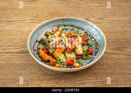 Caesar-Salat mit frischen Zutaten, geteilten Kirschtomaten und Schnittlauch mit Balsamico-Essig auf einem blauen, tiefen Teller Stockfoto