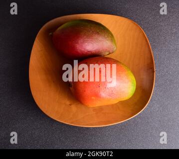 Zwei bunte Mangos und ein Holzteller Stockfoto