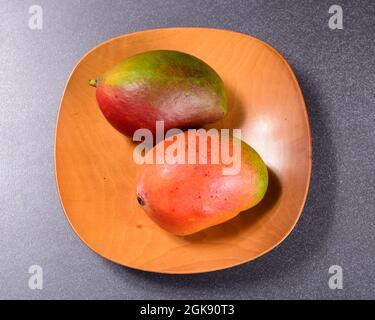 Zwei bunte Mangos und ein Holzteller Stockfoto