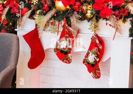 Leuchtend bunte rote Socken für Weihnachtsmann-Geschenke, die am weißen Kamin mit Weihnachtsdekorationen hängen. Traditionelle Weihnachts- und Neujahrsfeier Stockfoto