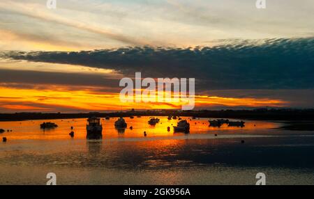 Unglaublicher Sonnenuntergang mit Fischerbooten, die sich im Ozeanwasser spiegeln und riesigen Wolken, die eine dramatische Atmosphäre schaffen Stockfoto