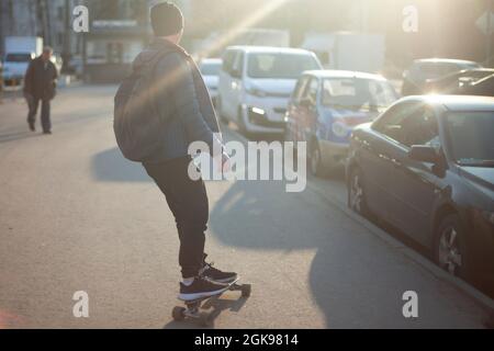 Der Typ auf dem Skateboard in der Sonne. Umweltfreundlicher Transport in der Stadt. Der Mann rollt durch die Stadt. Der Typ fährt auf einem gefährlichen Longboard Stockfoto