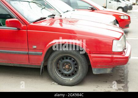 Rotes deutsches Auto auf dem Parkplatz. Rad auf dem Transport. Das Auto wird in einer Reihe mit anderen Autos geparkt. Helle Farbe. Seitenansicht des Fahrzeugs. Stockfoto