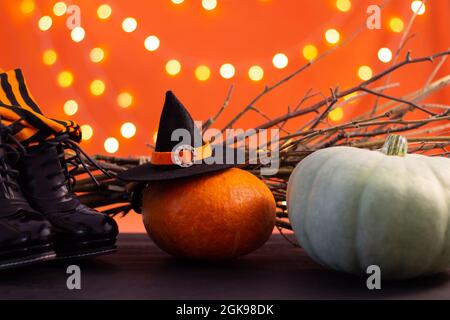 Hut, Stiefel, Strümpfe einer Hexe mit Ästen und Kürbissen auf orangefarbenem Hintergrund mit Bokeh. Halloween. Speicherplatz kopieren. Stockfoto
