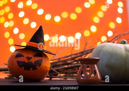 Hut einer Hexe mit Ästen, Kerze und Halloween Kürbissen auf orangefarbenem Hintergrund mit Bokeh. Speicherplatz kopieren. Stockfoto