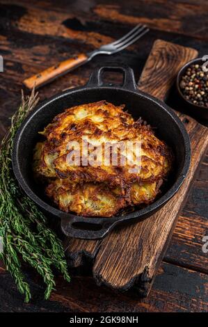 Gebratene Kartoffelpfannkuchen oder Krapfen mit Kräutern in einer Pfanne. Dunkler Holzhintergrund. Draufsicht Stockfoto