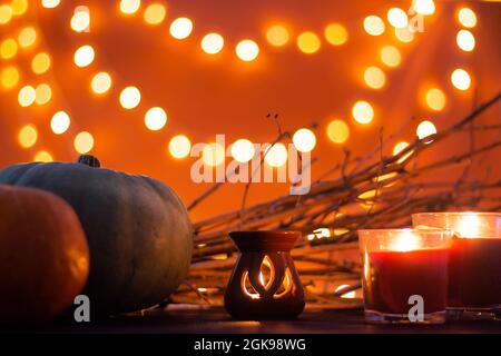 Zweige, Kerze und Halloween Kürbisse auf orangefarbenem Hintergrund mit Bokeh. Speicherplatz kopieren. Stockfoto