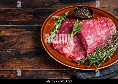 Zwei Lappen oder Flanken rohes Rindfleisch Steaks auf einem rustikalen Teller mit Kräutern. Dunkler Holzhintergrund. Draufsicht. Speicherplatz kopieren Stockfoto