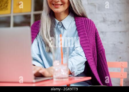 Lächelnde reife Frau arbeitet auf einem Laptop, der am Farbtisch auf der Cafeterrasse sitzt Stockfoto