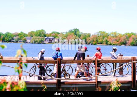 Richmond Hill, Ontario, Kanada-24,2021. Mai: Gruppe von Radfahrern, die Schutzmasken tragen, Radfahren, entlang der Brücke im Park in der Nähe des Sees wandern. Stockfoto