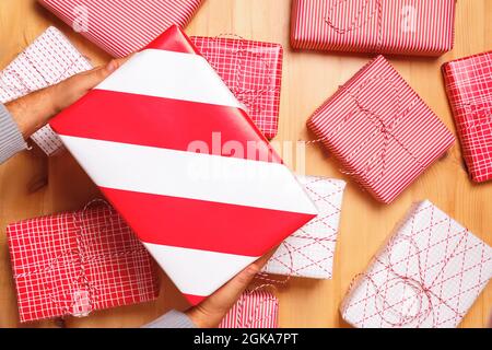 Nahaufnahme von männlichen Händen halten eine Weihnachtsbox mit einem Geschenk auf dem Hintergrund vieler Geschenke. Draufsicht. Stockfoto