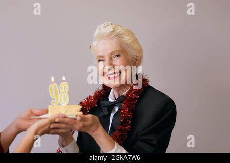 Happy fröhlich stilvolle achtundneunzig Jahre alte Frau in schwarzem Anzug feiert ihren Geburtstag mit Kuchen. Lifestyle, positiv, Mode, Stilkonzept Stockfoto