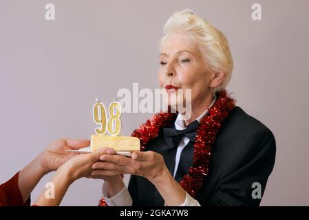 Happy fröhlich stilvolle achtundneunzig Jahre alte Frau in schwarzem Anzug feiert ihren Geburtstag mit Kuchen. Lifestyle, positiv, Mode, Stilkonzept Stockfoto