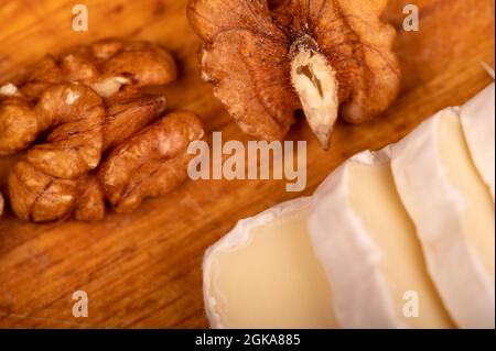 Geschnittene Kamembert- und Walnusskerne auf einem Holzschneidebrett, Nahaufnahme, selektiver Fokus Stockfoto