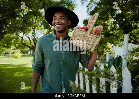 Gemischtes Rennen männlichen Landwirt zu Fuß im Freien hält Gemüskorb Stockfoto