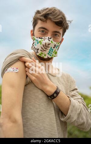 Porträt eines kaukasischen jungen Mannes mit Arm und Coronavirus-Impfpflaster. Stockfoto