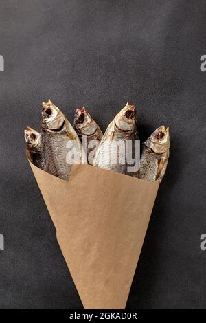 Bouquet von salziger, luftgetrockneter Kakerlake in Papierverpackung auf grauem Hintergrund Stockfoto