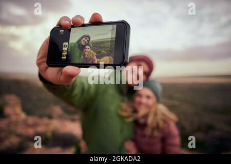 Nahaufnahme der männlichen Hand, die das Smartphone hält, das nach der Wanderung mit der Freundin Selfie auf dem Berg gemacht hat Stockfoto