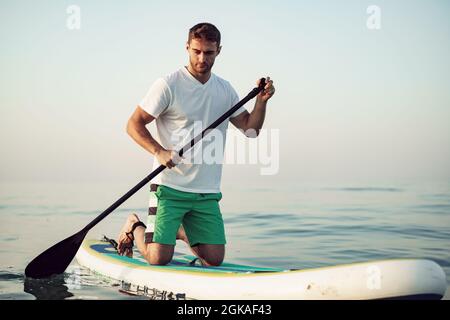 Junger Mann in T-Shirt und Shorts, der auf dem SUP-Board schwimmt Stockfoto