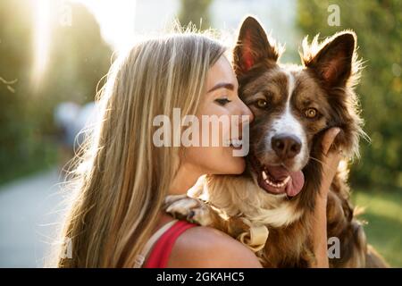 Nahaufnahme eines Porträts einer jungen Frau, die ihren Hund im Park küsst Stockfoto